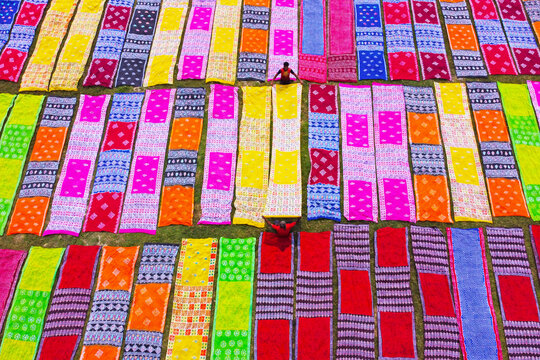 Aerial view of colorful sarees laid out to dry on the grass with a worker walking among them in Narayanganj, Dhaka, Bangladesh.