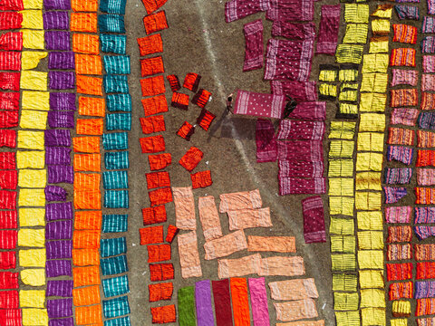 Aerial view of colorful fabrics laid out to dry on the ground with workers walking among them in Narayanganj, Dhaka, Bangladesh.