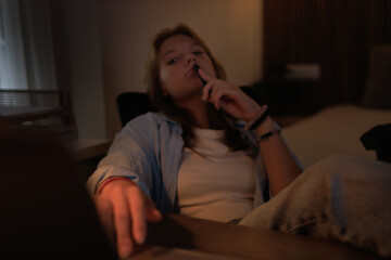 Obraz premium Young woman student focused and engaged in deep thought while studying or working late at night, holding a pen near her mouth, wearing casual clothes at a desk