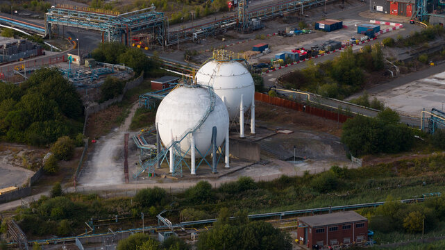 Aerial view of the INEOS Electrochemical Solutions facility featuring large white spherical gas storage tanks and industrial piping surrounded by vegetation in Runcorn, England, United Kingdom.