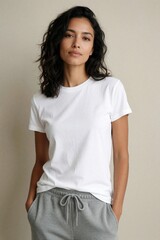 Fototapeta premium Woman wears plain white tee and grey sweatpants. She stands casually indoors with hands in pockets. Simple outfit for everyday wear. Clean backdrop focuses on attire.