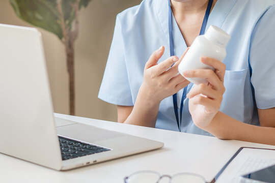 Female doctor or pharmacist holding white medicine bottle explaining supplement usage to patient via laptop video call telehealth medical online consultation concept close up side view