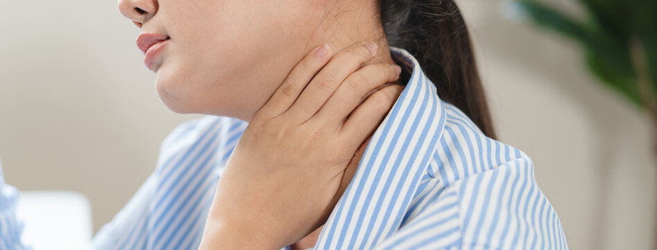 Close up Asian woman hand touching neck feeling painful suffering from sore throat office syndrome neck pain thyroid problem cervical spine injury massage or medical health care concept
