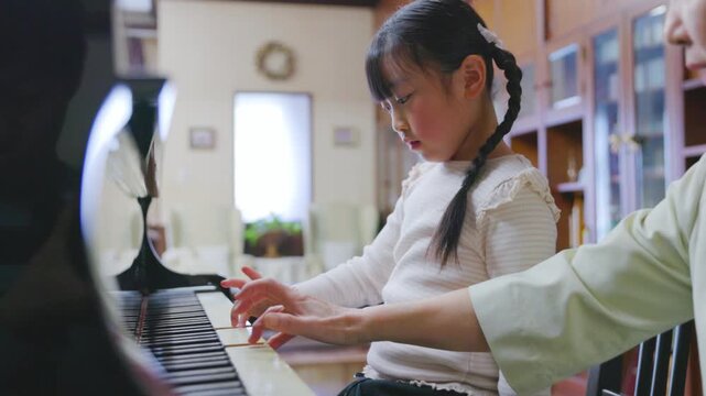 女性の先生と一緒にピアノを弾く女の子