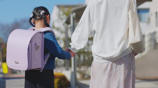 ランドセルの女の子と手をつないで通学路を歩く母親の後ろ姿