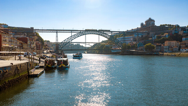 Aerial view of the iconic Dom Luis I Bridge spanning the Douro River with traditional rabelo boats and historic buildings along the waterfront in Porto, Porto District, Portugal.
