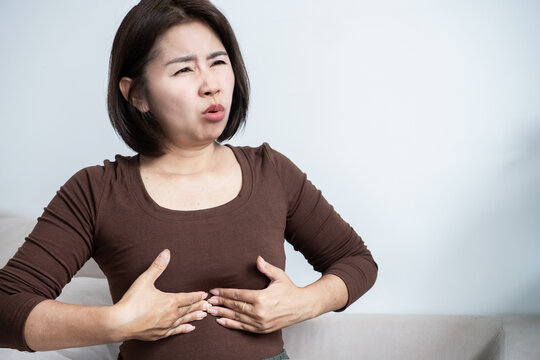 Asian woman suffering from heartburn, acid reflux, and chest pain touching her sternum. Stressed female feel pain from indigestion, gastritis, and stomach problem