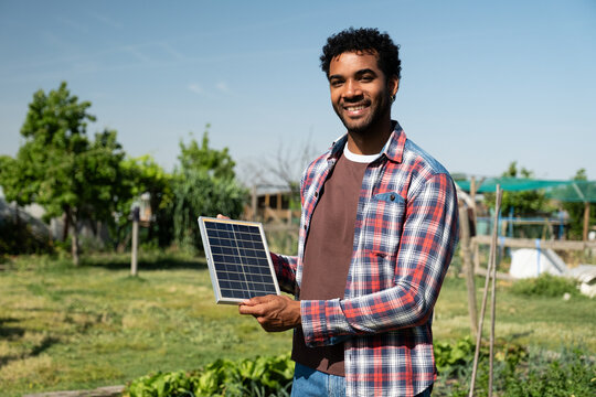 Smiling man holding a mini solar panel in a garden for sustainable power