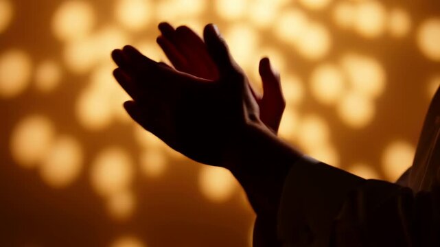 Silhouetted hands overlap in warm golden light with soft bokeh background, creating expressive close framed gesture and dramatic backlit mood for celebration, worship, praise, hope, emotion, and
