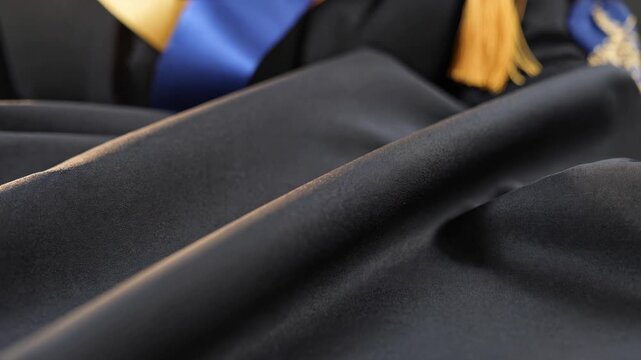 Close-up of black academic gown, tassel, and stole for graduation ceremony, showcasing success, achievement, and higher education for a graduate celebrating a diploma