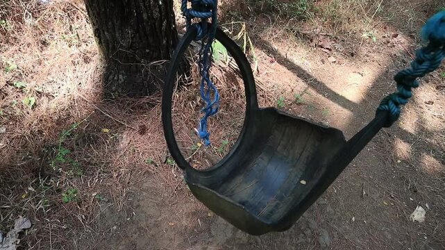 A homemade swing made from a recycled rubber tire hanging from a tree in the forest. perfect for concepts of childhood nostalgia, relaxation, freedom, and peaceful leisure.