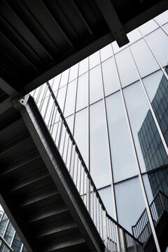 Metal staircases ascend against a glass facade reflecting city buildings. Geometric patterns create abstract urban scene, emphasizing modern architecture and industrial design.