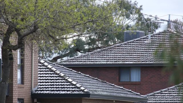Terracotta tiled rooftops of brick suburban homes with a TV antenna, air conditioning unit, and overhead power lines in Melbourne, Australia