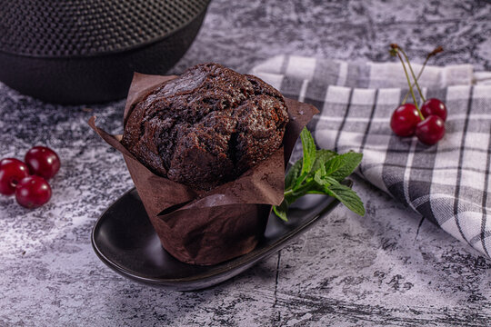 Chocolate muffin with cherries and mint on rustic surface