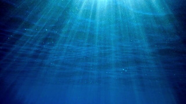 A slow-motion shot of an underwater sea background, sunlight penetrating and reflecting of sea surface. deep undersea. light rays shining through. Dark blue ocean surface seen from under water.