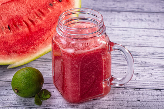 Fresh watermelon smoothie in glass mug with lime and mint on rustic wood table