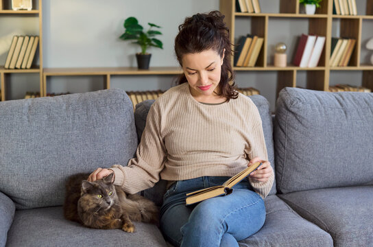Woman reading book beside cat on sofa. Tranquil home scene highlighting relaxing pet companionship and leisure. Ideal for lifestyle and wellness. Cozy relaxation and companionship concept.