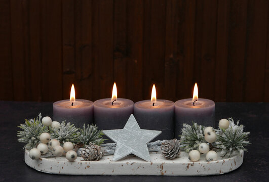 Fourth Sunday of Advent: Advent arrangement with berries, twigs, and four lit candles against a wooden background, with space for text.