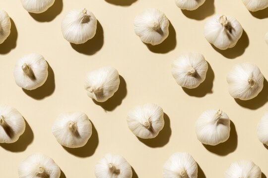 Whole white garlic bulbs arranged in a flat-lay pattern on a warm cream-beige surface, showcasing their natural textures and organic appearance with varying orientations