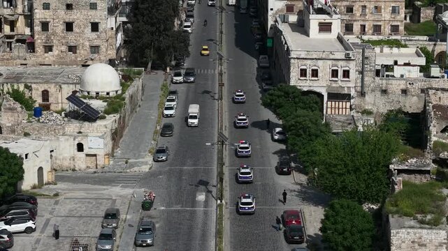 Aerial drone view of tourism police vehicles and officers in Aleppo, Syria. Syrian tourism police convoy driving through city streets after the fall of Bashar al-Assad. New Syrian government security 