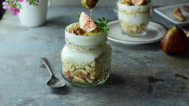Honey dripping on fresh organic fig sliced inside healthy yogurt parfait jar with granola on table. Close up delicious artisanal breakfast snack concept