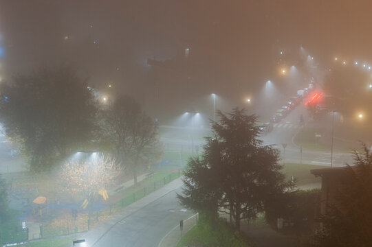 Scena notturna con strada curva, alberi, parco giochi e luci diffuse dalla nebbia. Ideale per temi citt&agrave;, atmosfera, notte, introspezione, paesaggio urbano e fotografia ambientale.