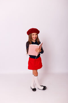 ull length portrait of happy little girl in red beret holding open notebook on white background