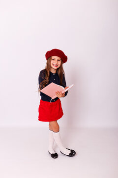 ull length portrait of happy little girl in red beret holding open notebook on white background
