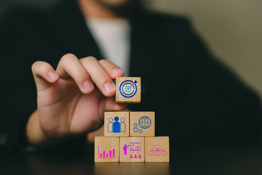 A professional holding a small wooden block with a target symbol above other stacked blocks representing analysis, planning, growth, and strategic success.
