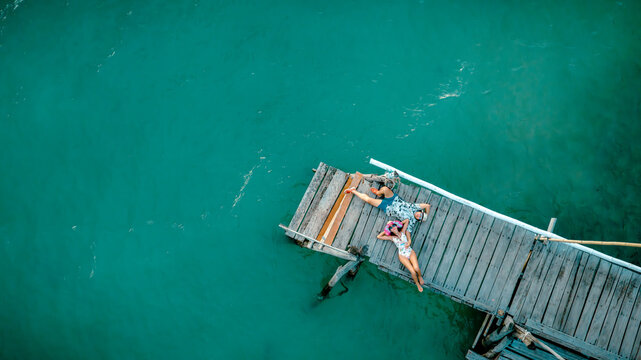 Top aerial view of couple tourist in happiness and relax moment on wooden pier, enjoy the summer trip in tropical island