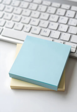 Stack of blank blue and yellow sticky notes on a white desk with a blurred computer keyboard in the background, a blurred computer keyboard is visible in the background
