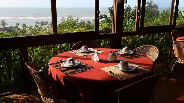 Breakfast table set with a stunning ocean view in charming Arraial d'Ajuda, Bahia, Brazil. Sunlight streams through large windows onto a cozy morning setup.