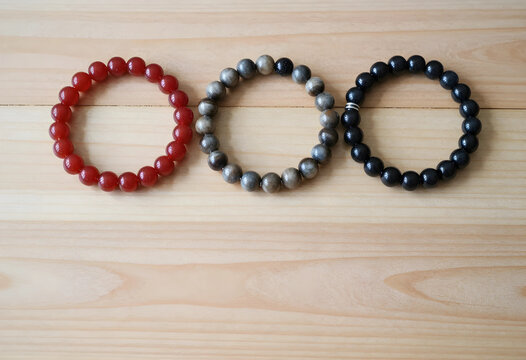 Three natural stone bead bracelets in red, gray, and black colors on a light wooden background