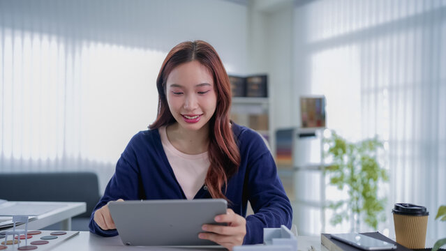 Young Asian furniture designer reviewing digital tablet in bright modern office with copy space