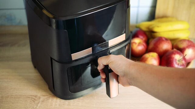 Inserting air fryer basket with raw french fries potato inside machine