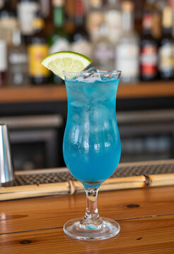 Blue hawaiian cocktail with lime garnish and ice on a wooden bar counter with blurred liquor bottles, the background features a blurred array of liquor bottles, a lively bar or restaurant setting