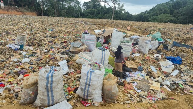 KENDARI, INDONESIA - JULY 24, 2026: A scavenger woman stands among large sacks filled with sorted recyclable plastic waste collected manually at the Puuwatu landfill site.