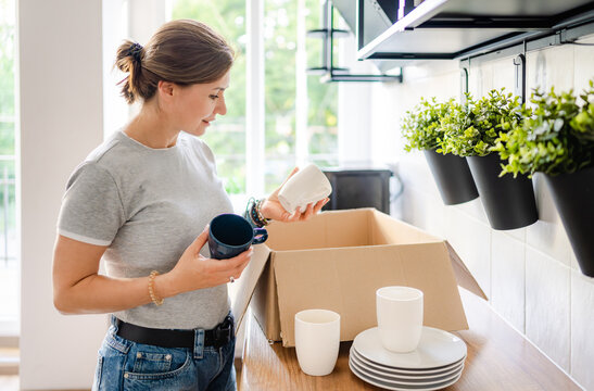 Woman takes ceramic mugs out of cardboard box in sunny kitchen setting