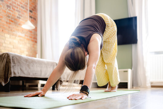 Woman in comfortable pajamas performs yoga stretching in living room during the morning