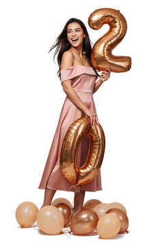 Happy woman in pink dress holding golden number twenty balloons for birthday anniversary celebration with balloons