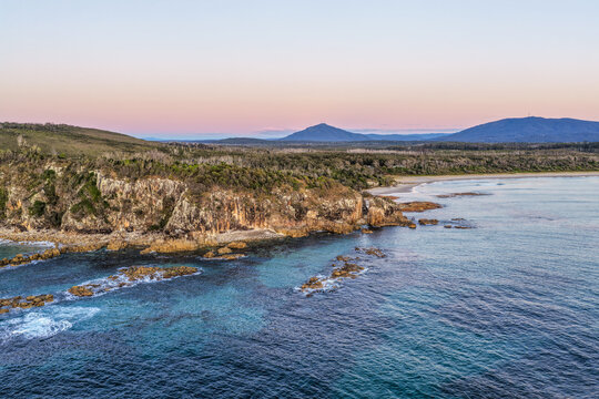 Aerial view of Diamond Head Beach and headland surrounded by ocean and coastal landscape beneath soft pastel morning light at Diamond Head.
