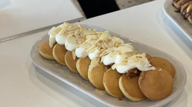 Chef Serves Mini Pancakes with Cream and Almond Flakes Beside Iced Drinks and Banana Dessert