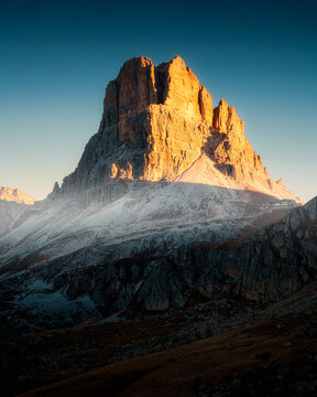 Dolomites mountain peak glowing in golden morning sunlight with clear blue sky in Italy