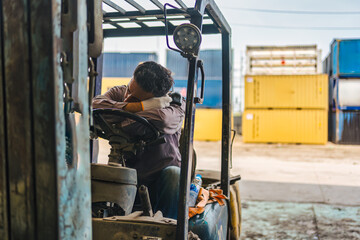 Fototapeta premium Exhausted logistics worker sleeping on forklift steering wheel in freight yard cargo container depot