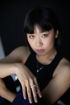 Chinese girl poses with her hand outstretched in front of her, shows a pearl ring , her face in blur, black background.