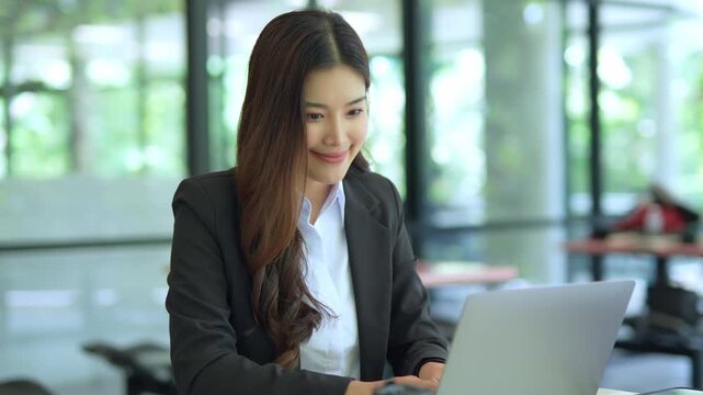  Asian businesswoman working at desk using laptop and notebook talking to client or office building, slow motion footage