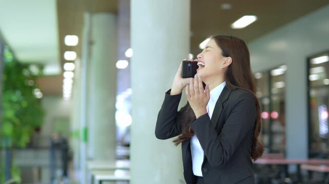 Asian businesswoman using mobile phone, texting and chatting with her smartphone with colleagues outside modern office.