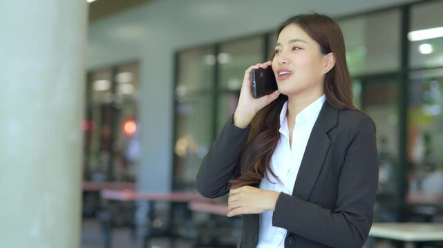 Asian businesswoman using mobile phone, texting and chatting with her smartphone with colleagues outside modern office.