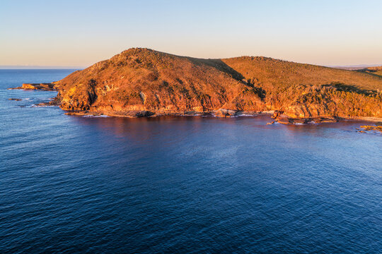 Aerial view of Indian Head surrounded by the blue waters of the Pacific Ocean, featuring a rugged rocky coastline, native coastal vegetation and waves breaking along the shoreline near Diamond Head 