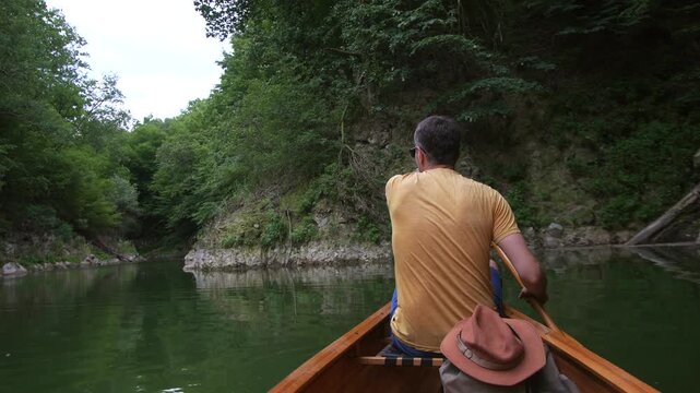 Man paddling wooden canoe on peaceful forest lake